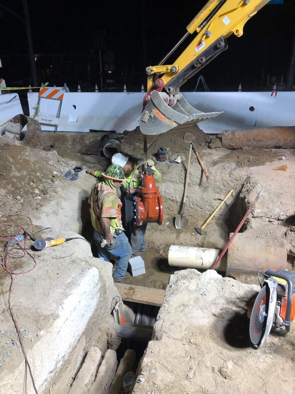 Field crews installing a valve in an open utility trench at night